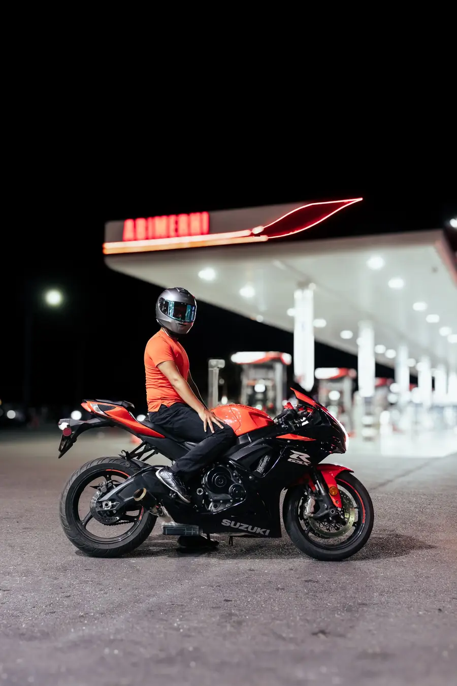 Motociclista em moto parada em posto de gasolina à noite
